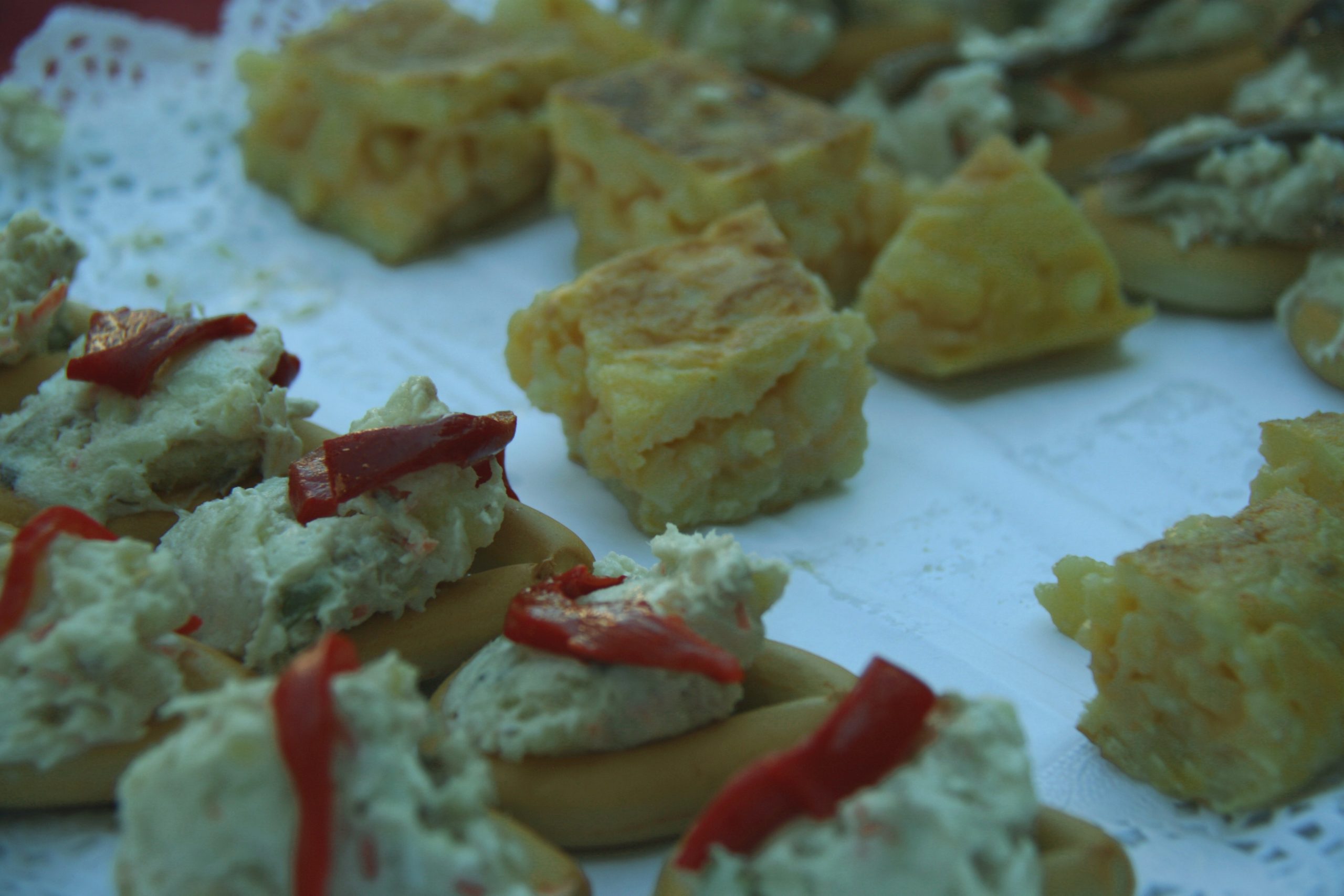 Small plates of potato tortilla squares and topped bread bites on a lace-covered tray