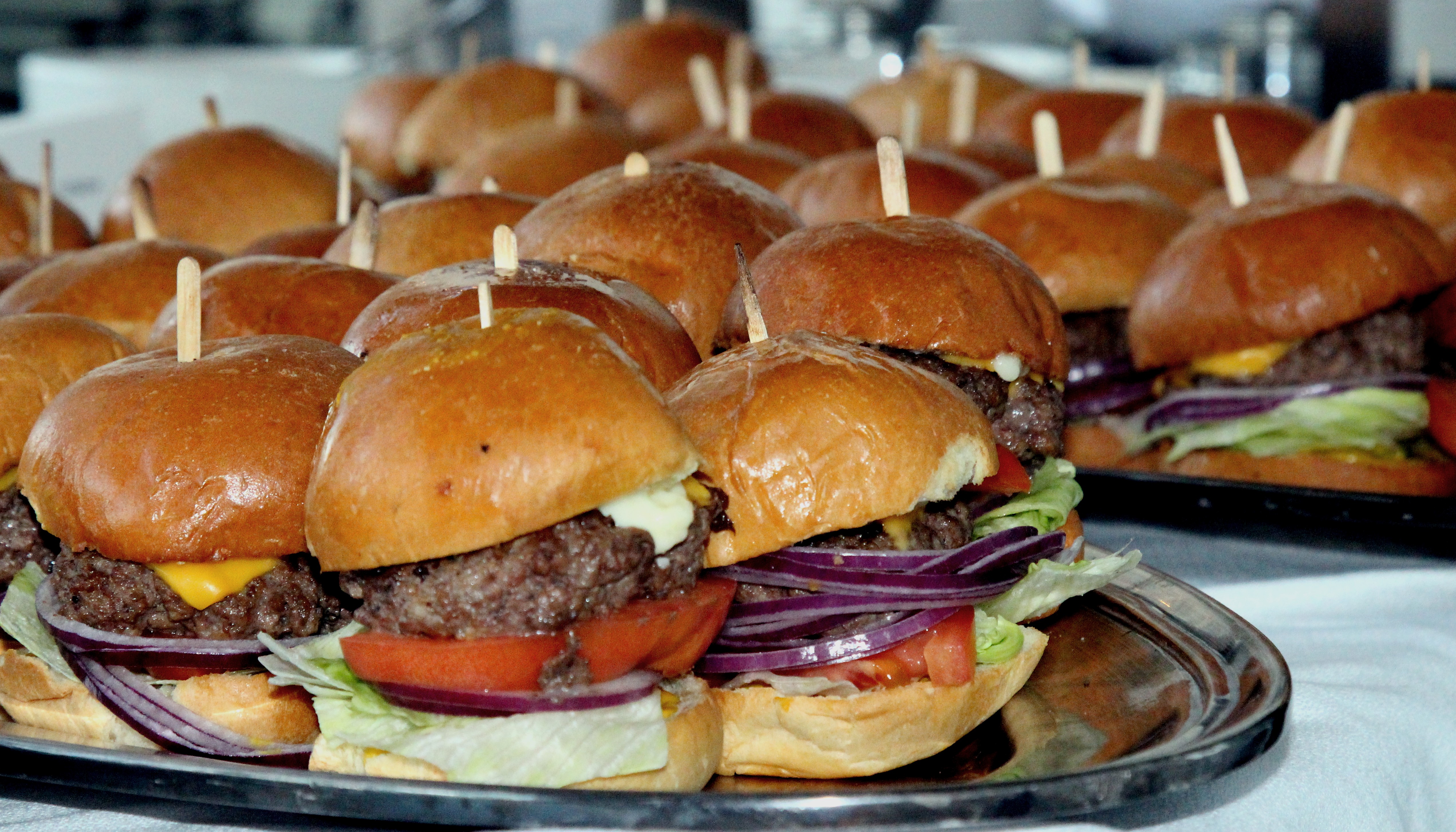 Rows of mini cheeseburger sliders held with wooden picks on a serving tray