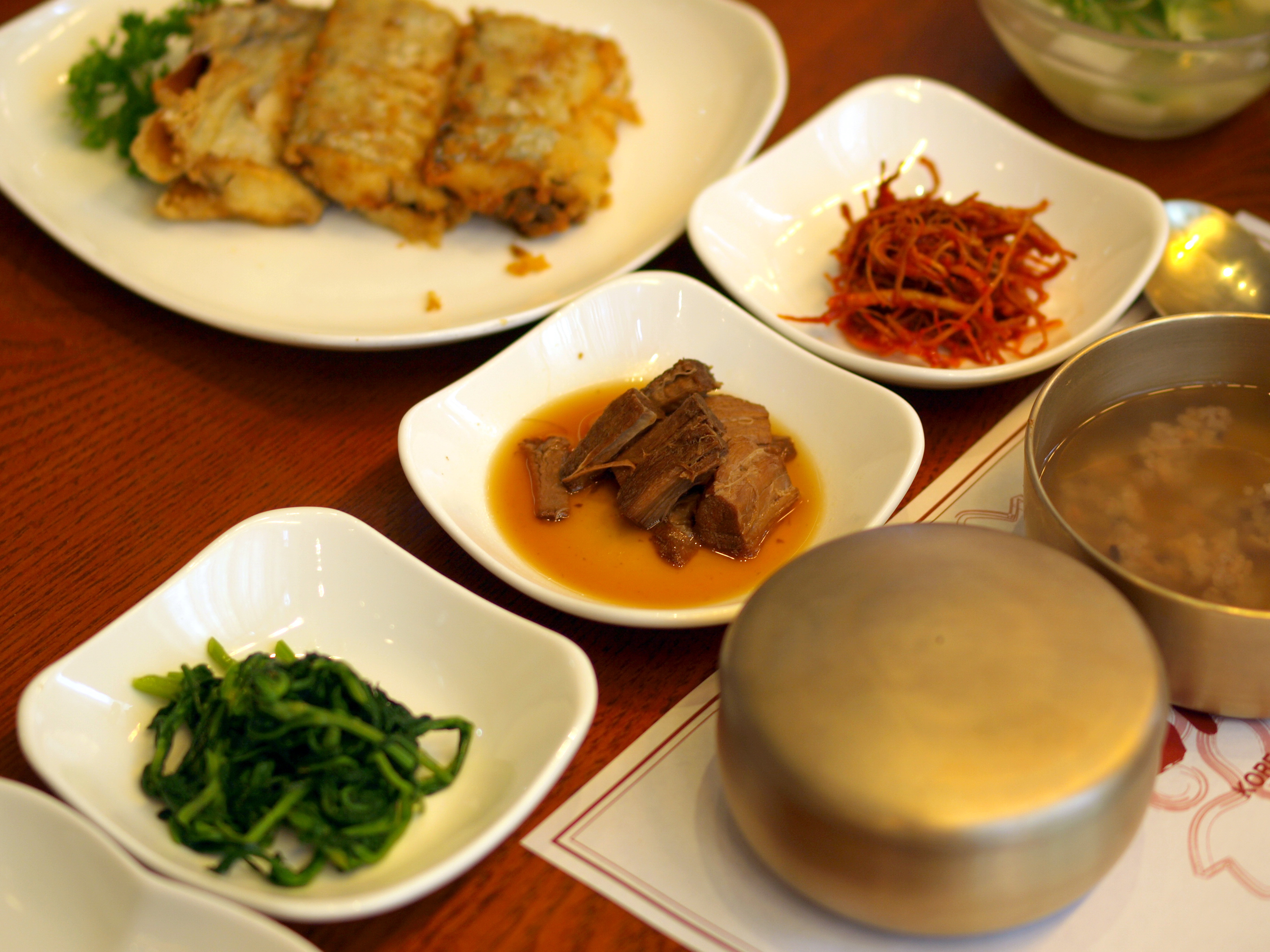 Several small shared side dishes and a covered rice bowl on a restaurant table
