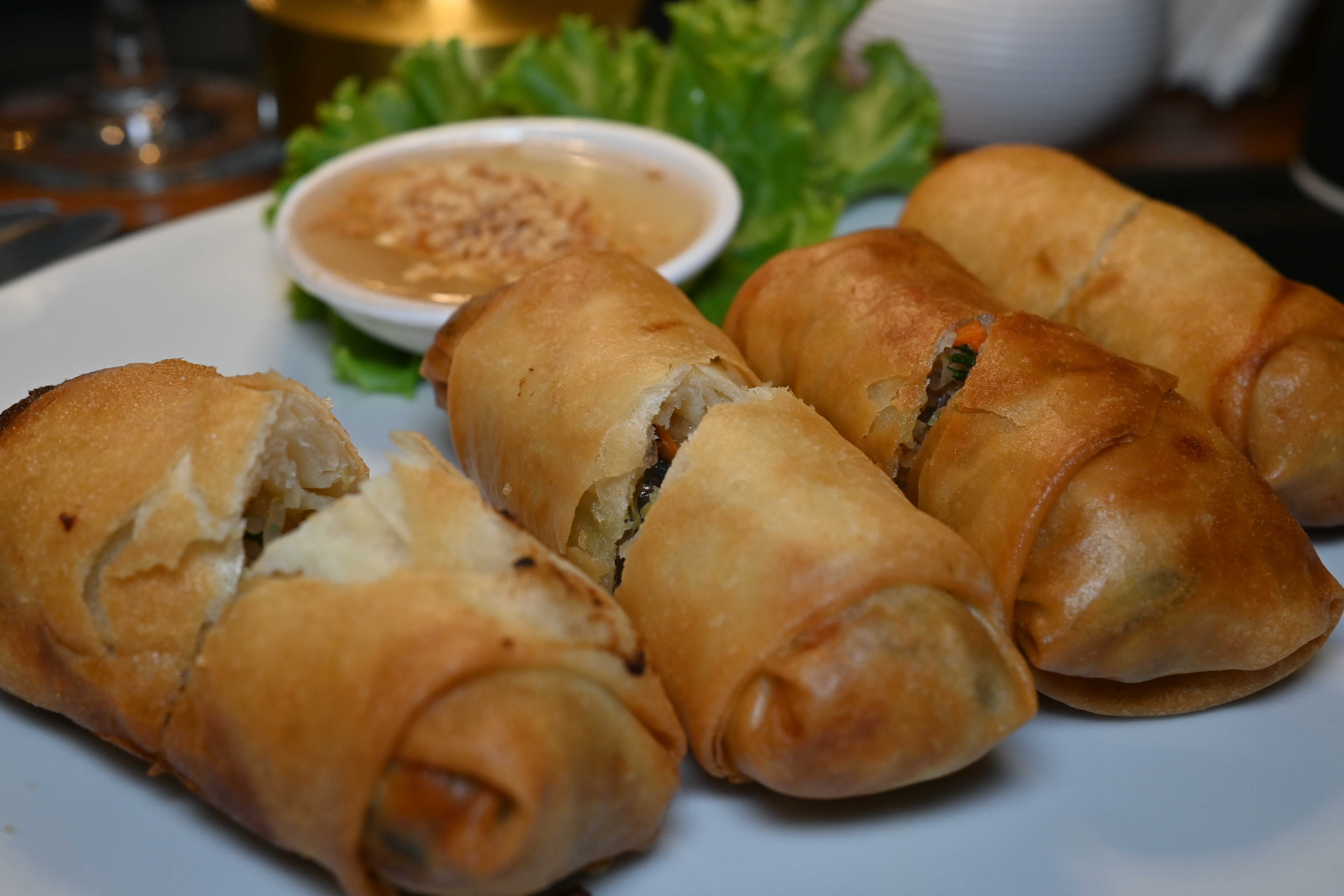 Crispy spring rolls cut open beside a dipping sauce and lettuce