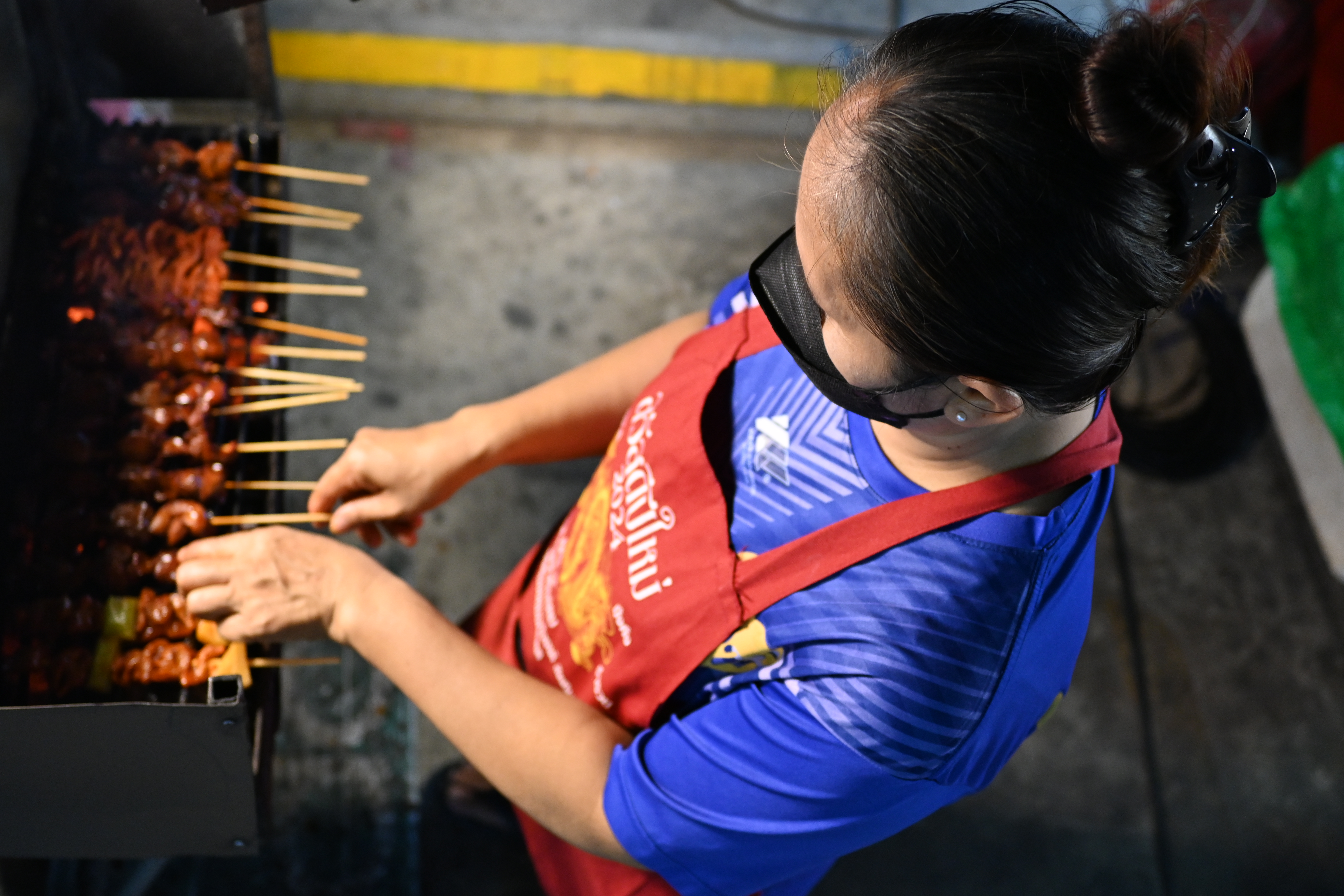 Overhead view of a vendor turning meat skewers on a charcoal grill