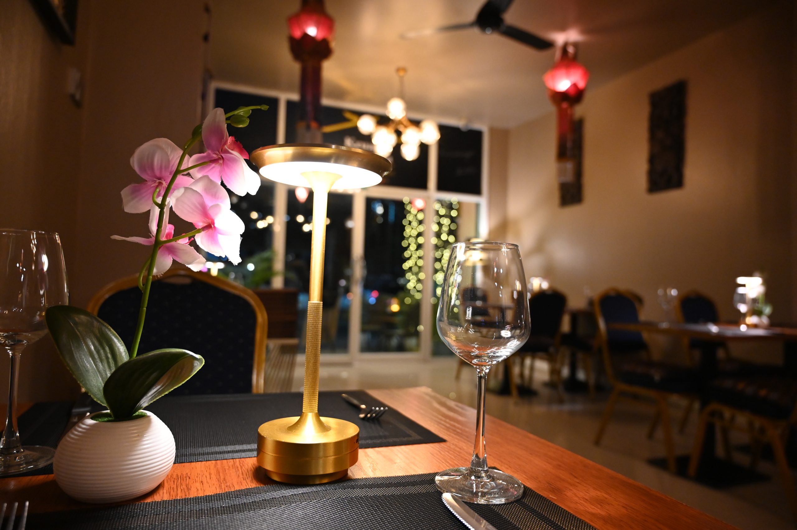 Quiet restaurant dining room in early evening with a table lamp, orchid and empty wine glass