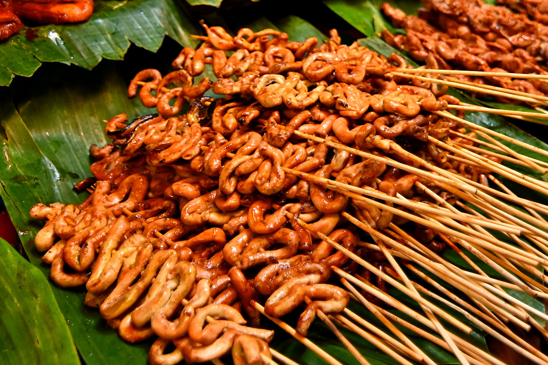 Grilled skewers piled on banana leaves at a street food stall