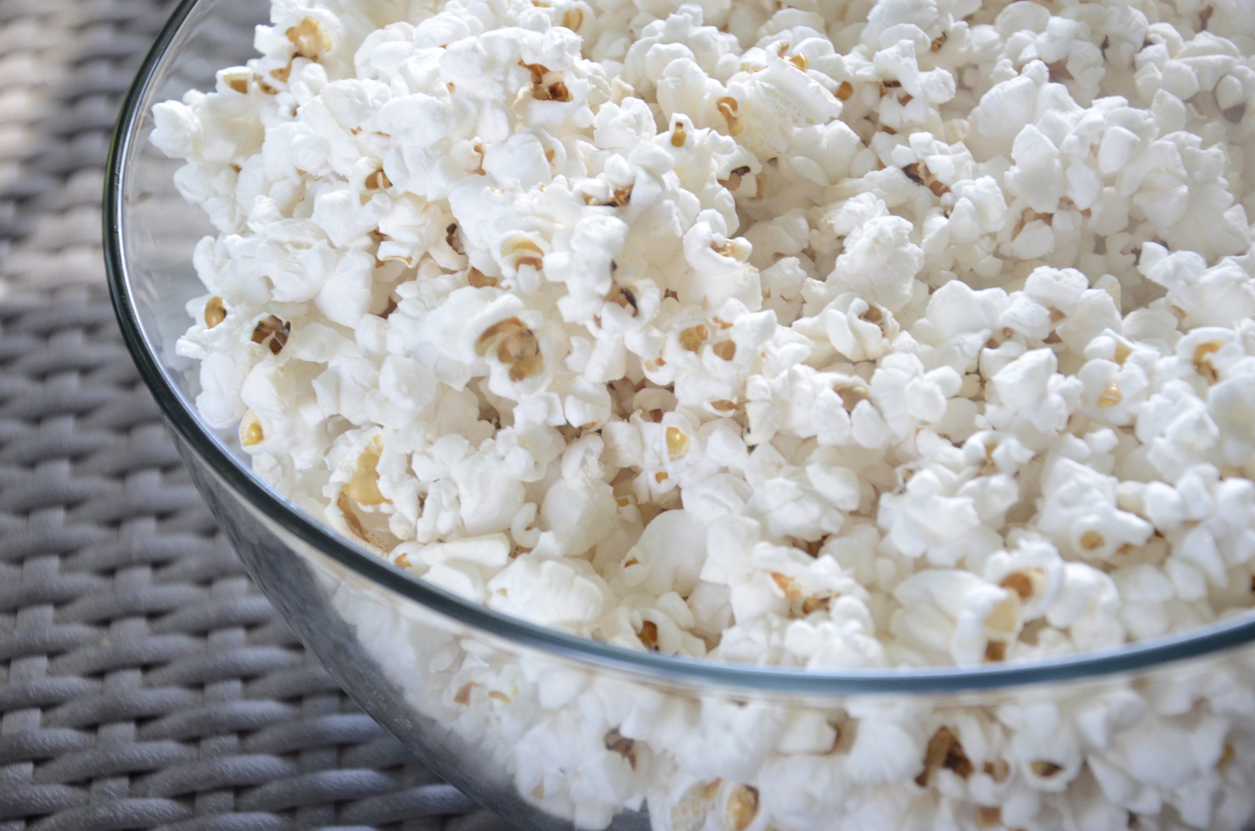 Glass bowl filled with freshly popped popcorn on a woven mat
