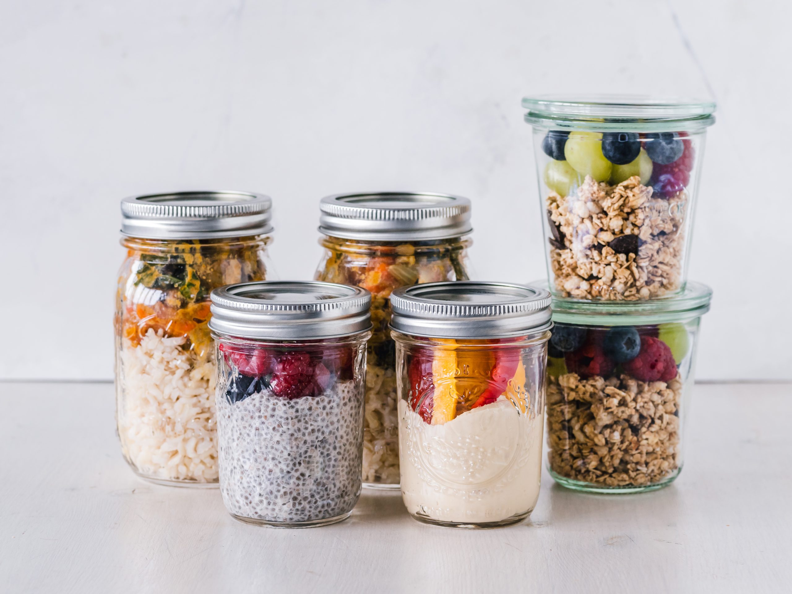 Glass jars of rice salad, chia pudding, yogurt and granola with fruit prepared for the week