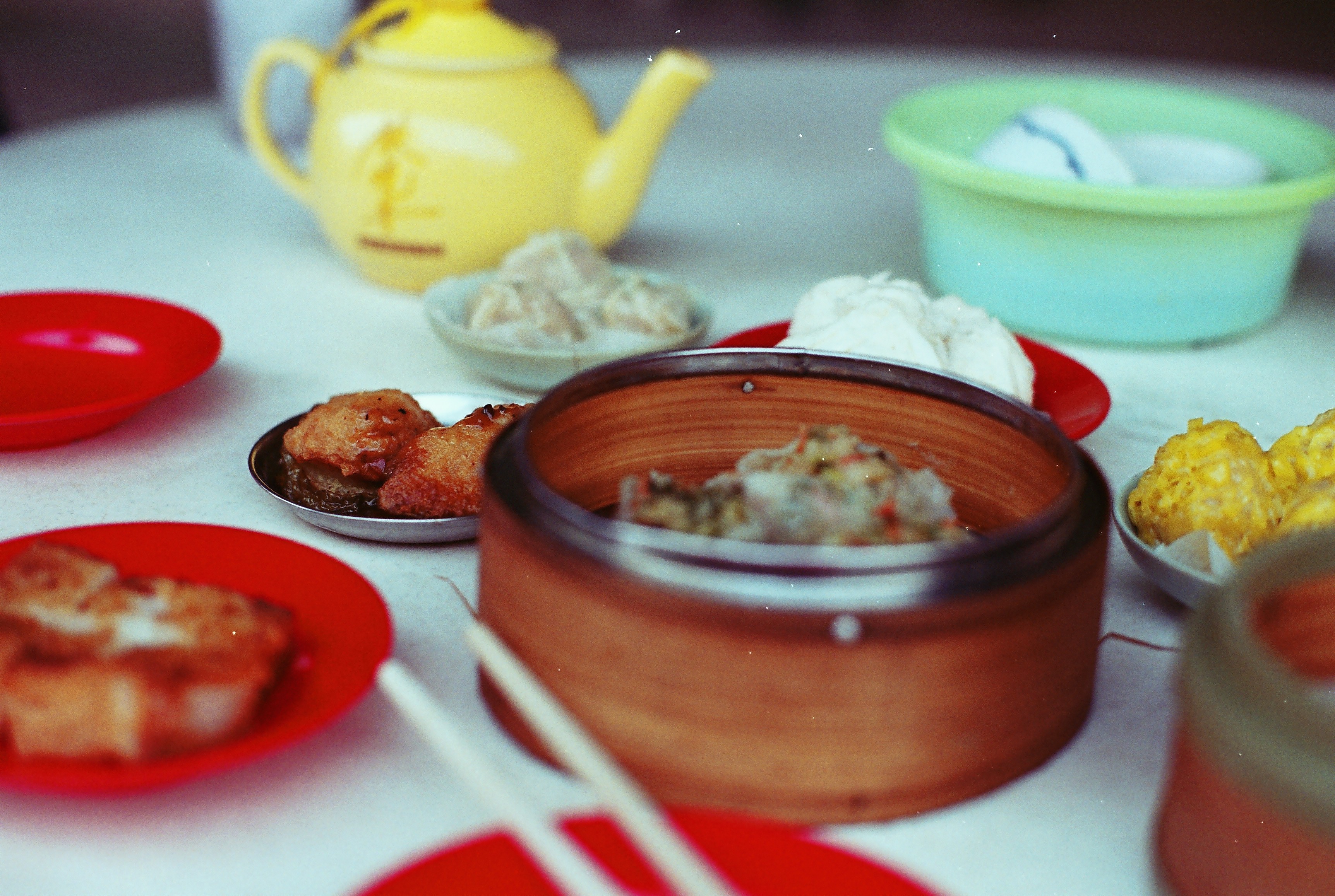 Bamboo steamer, small plates of dim sum and a teapot shared on a round table