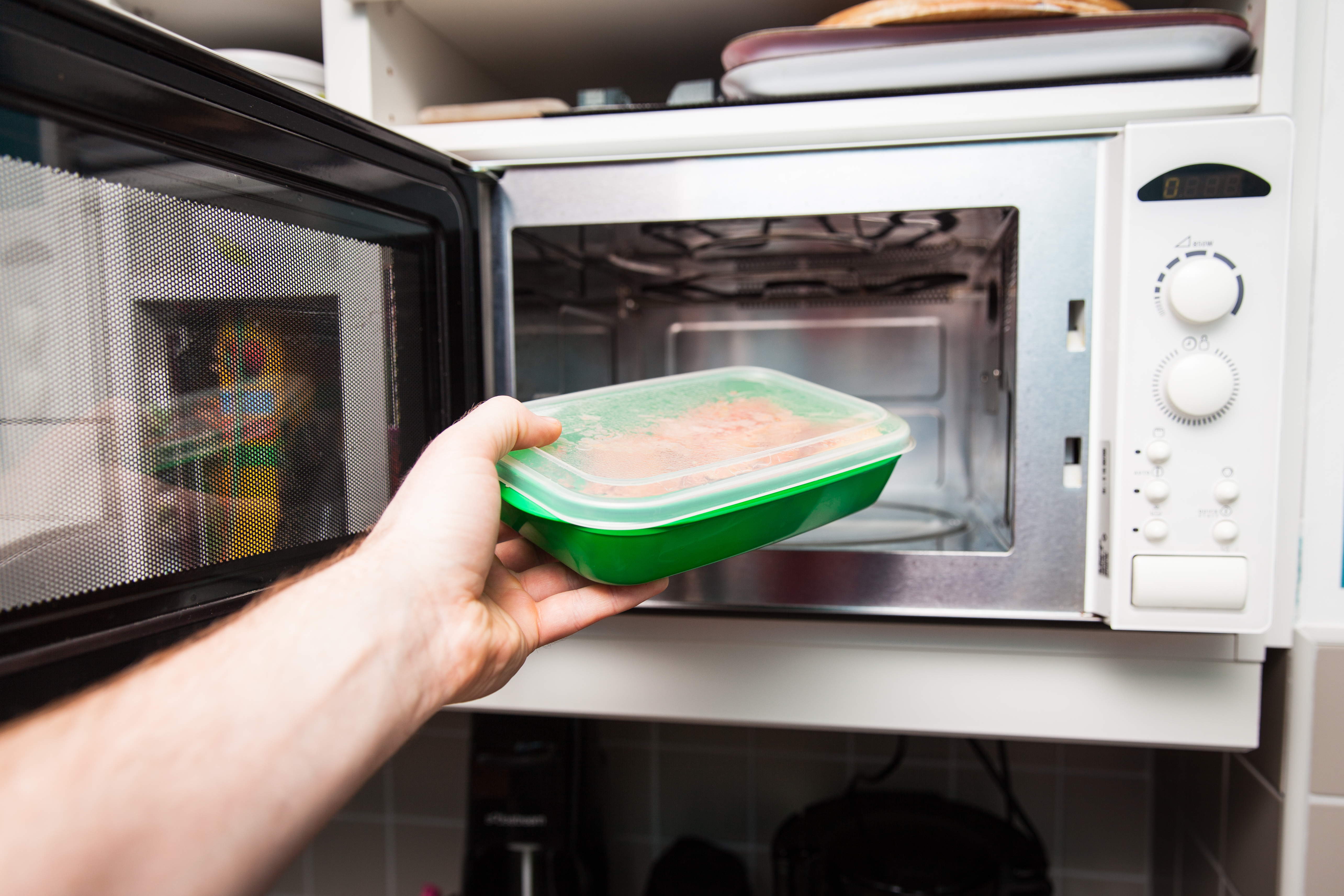Hand placing a lidded lunch container into an office microwave