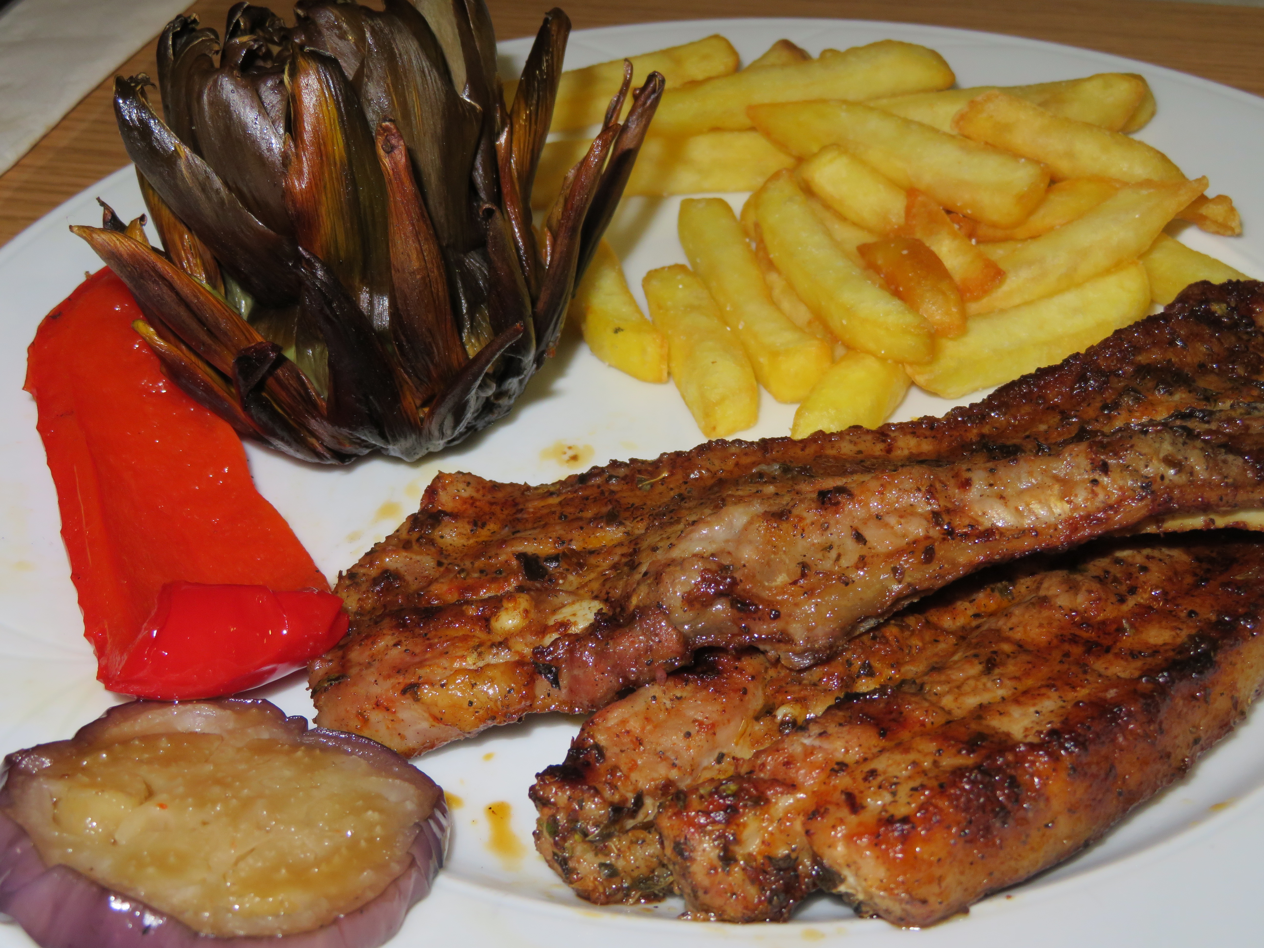 Grilled pork with fries, roasted pepper, eggplant and artichoke served as a set lunch main course