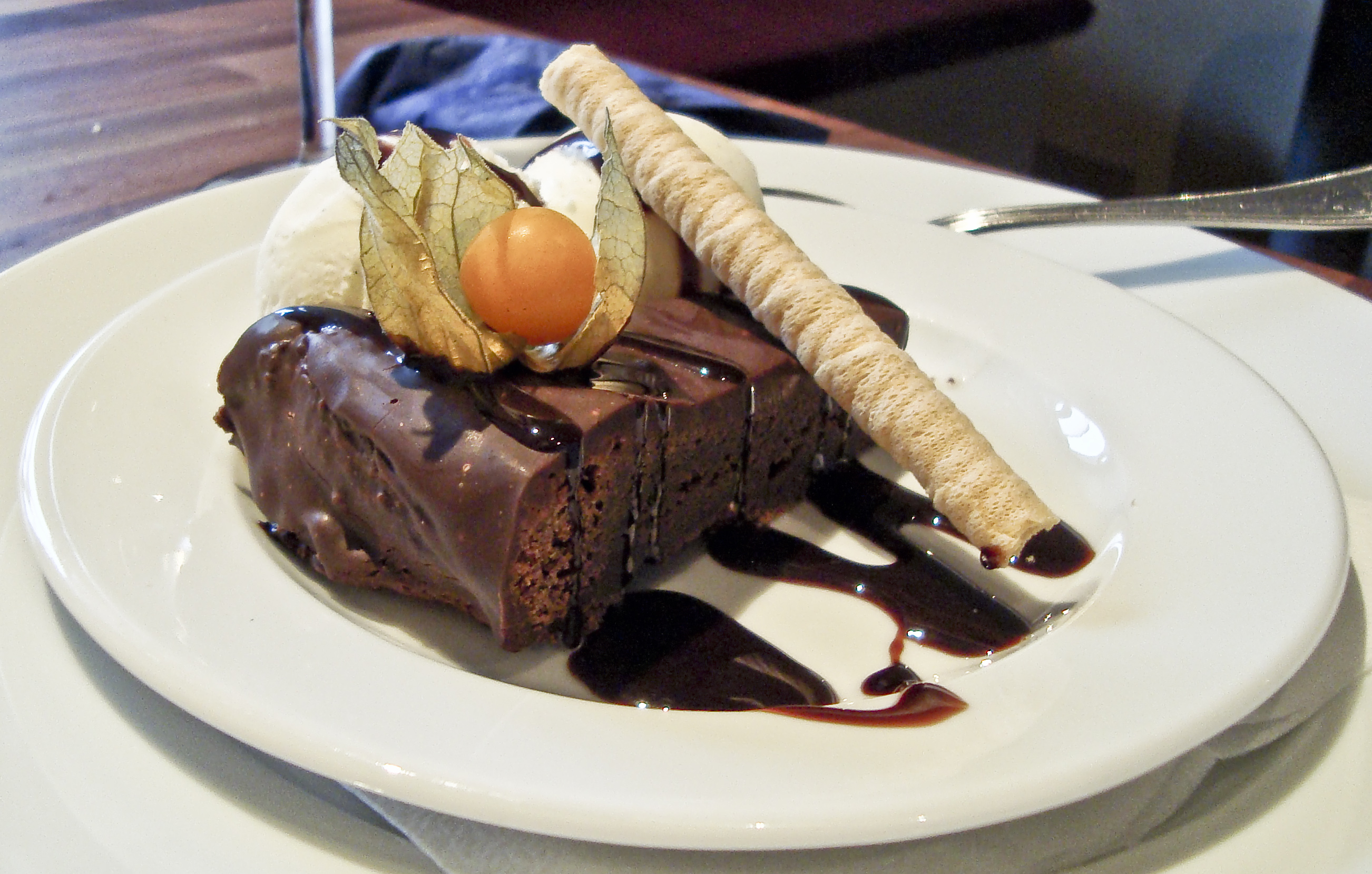 Slice of chocolate cake with vanilla ice cream, a wafer roll and a physalis on a white plate