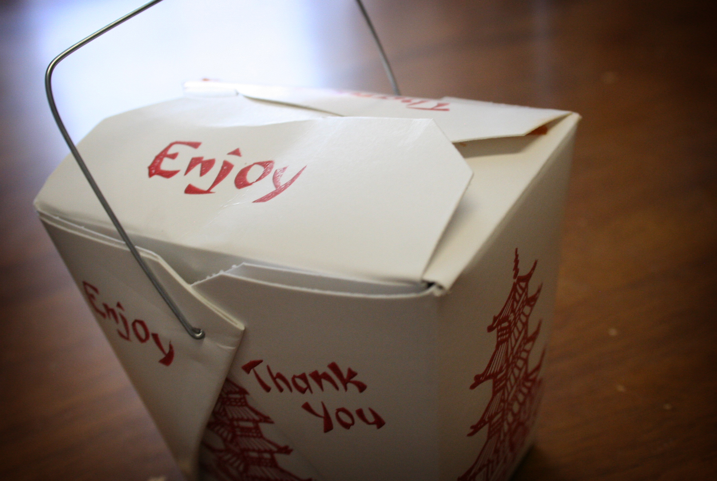 White folded paper takeout box with a wire handle on a wooden table