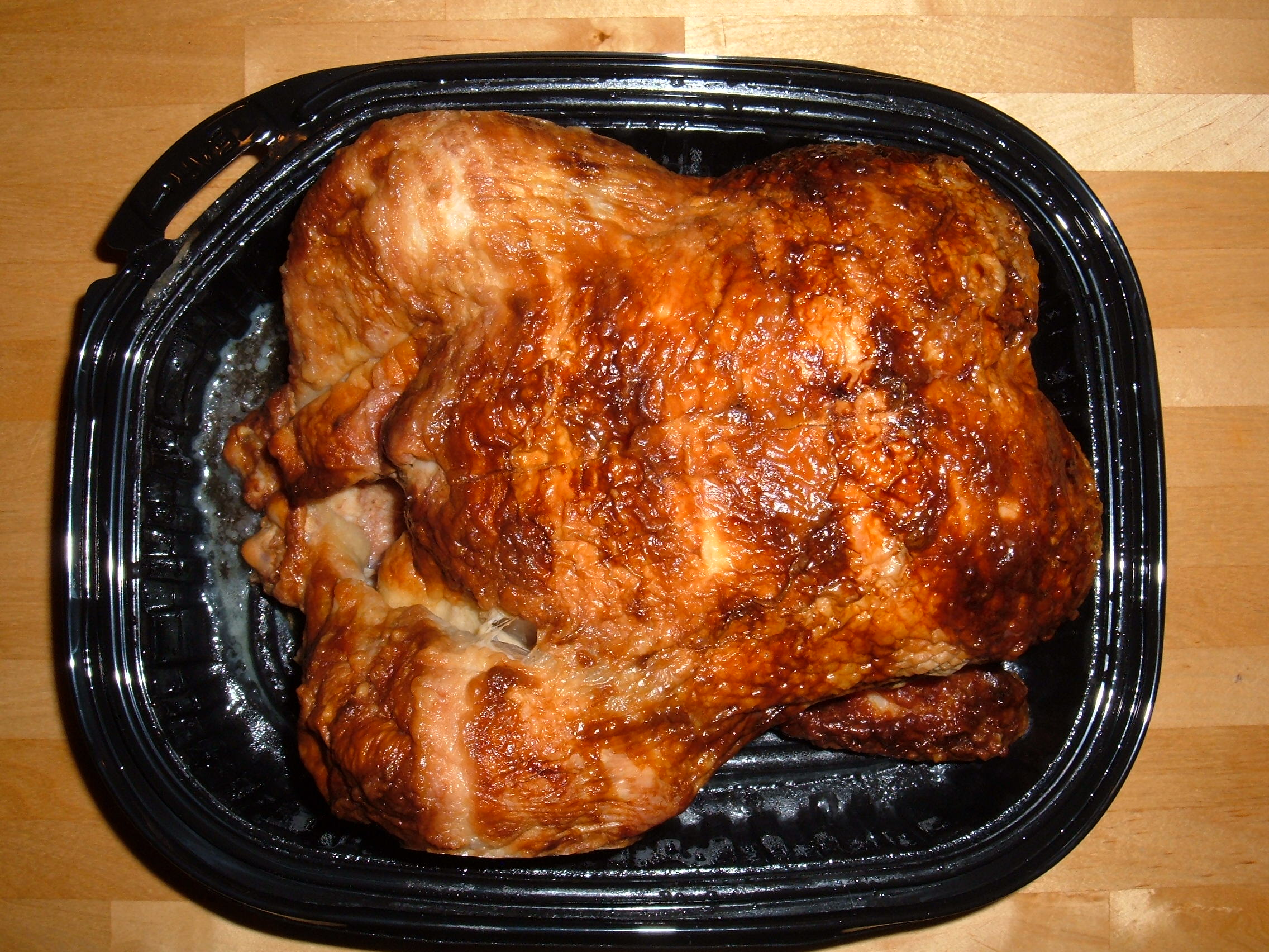 Whole rotisserie chicken in a black plastic container on a wooden counter