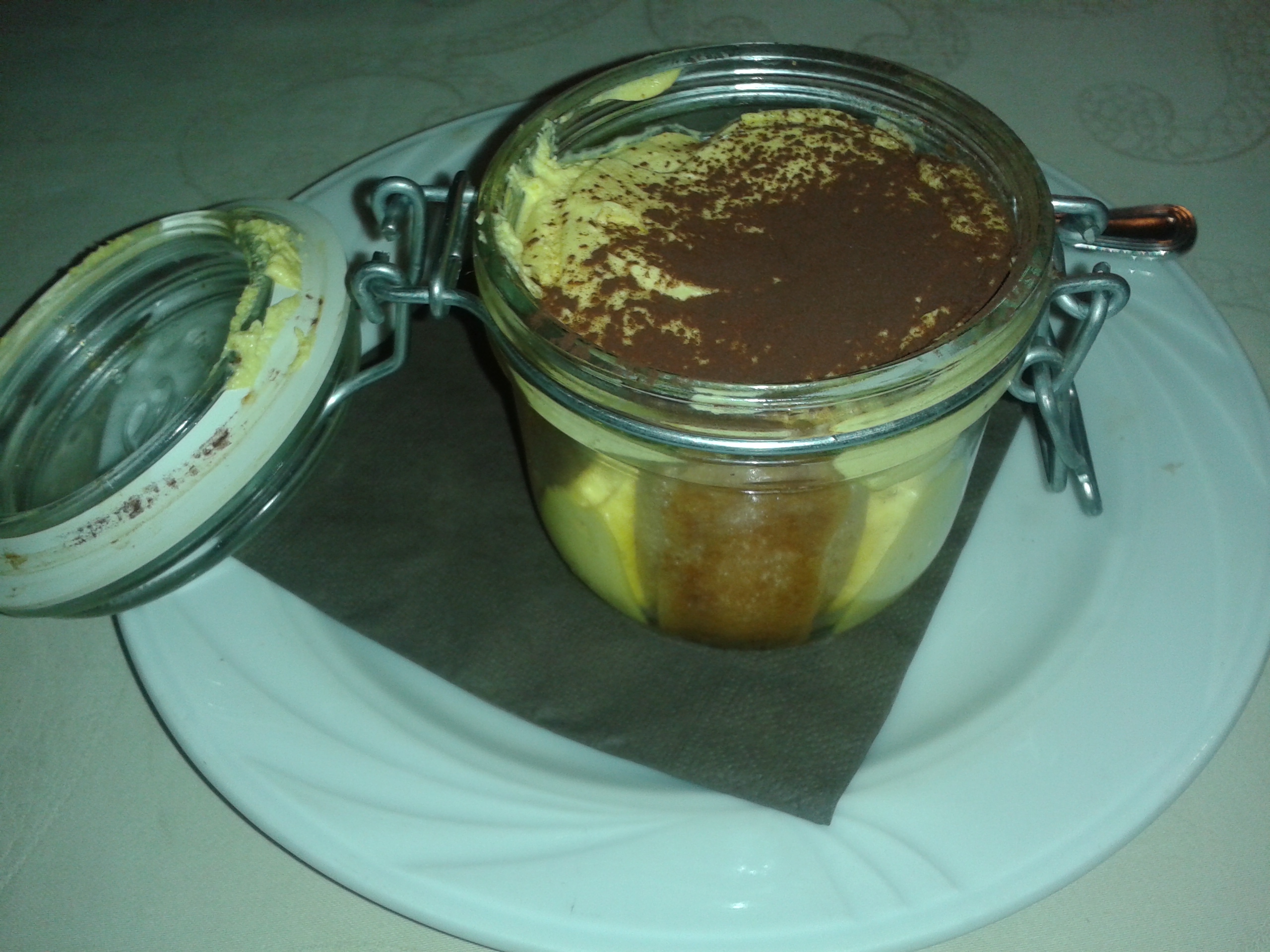 Tiramisu dusted with cocoa served in a clip-top glass jar on a white plate