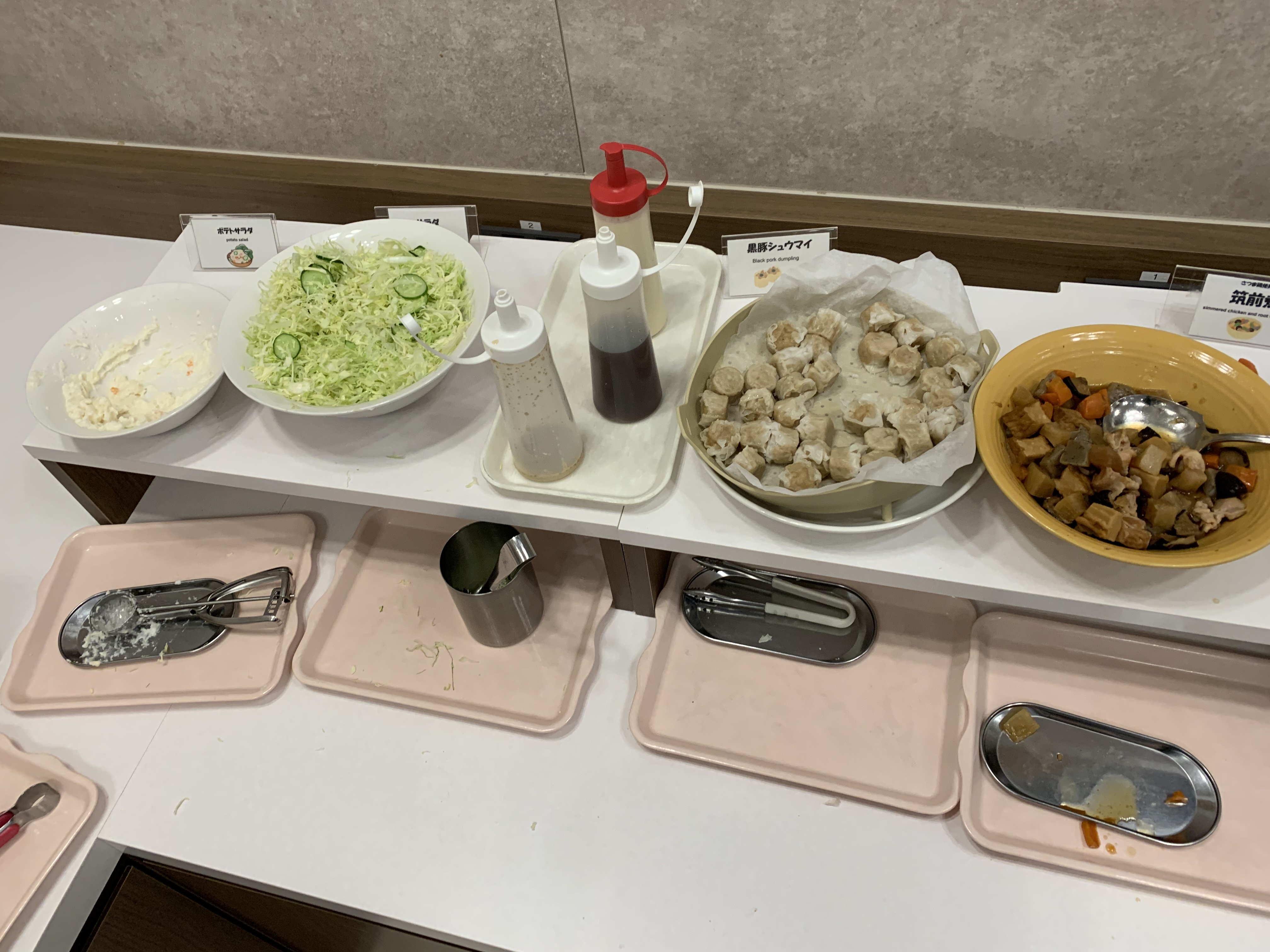 Buffet counter with bowls of salad, steamed dumplings and simmered vegetables beside serving trays