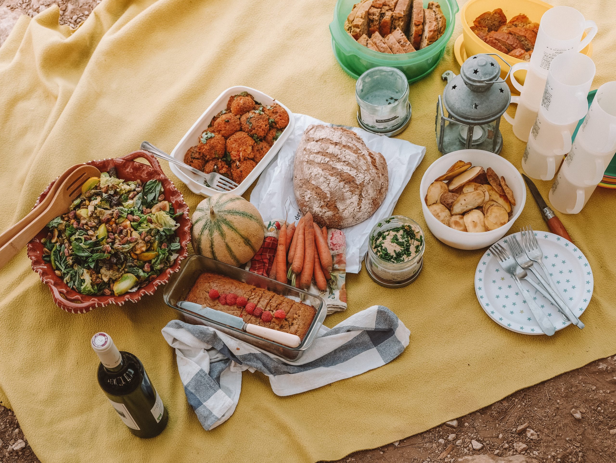 Picnic spread on a yellow blanket with salad, bread, carrots, melon, baked falafel and cake