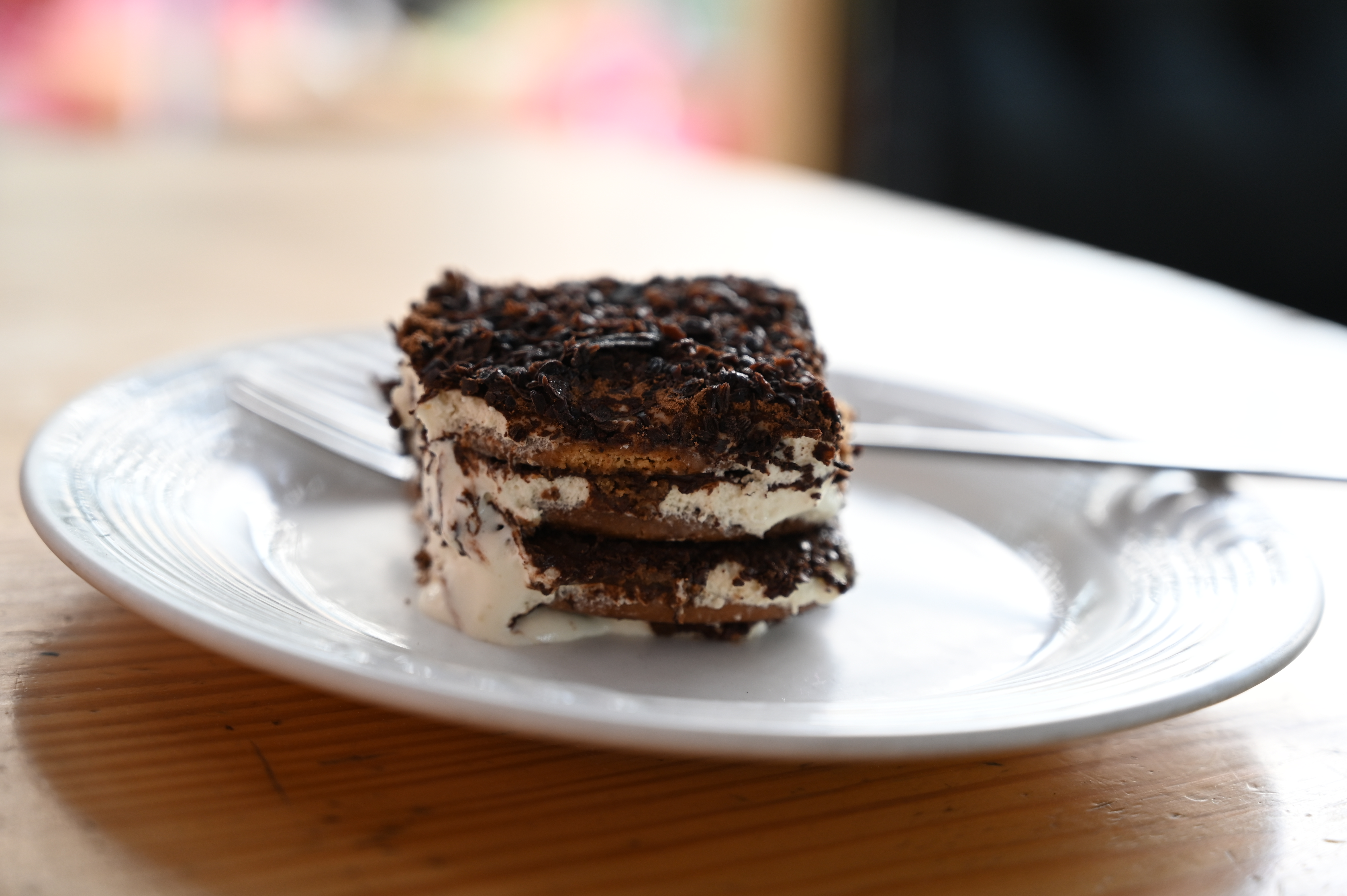 Square of layered tiramisu topped with grated chocolate on a white plate
