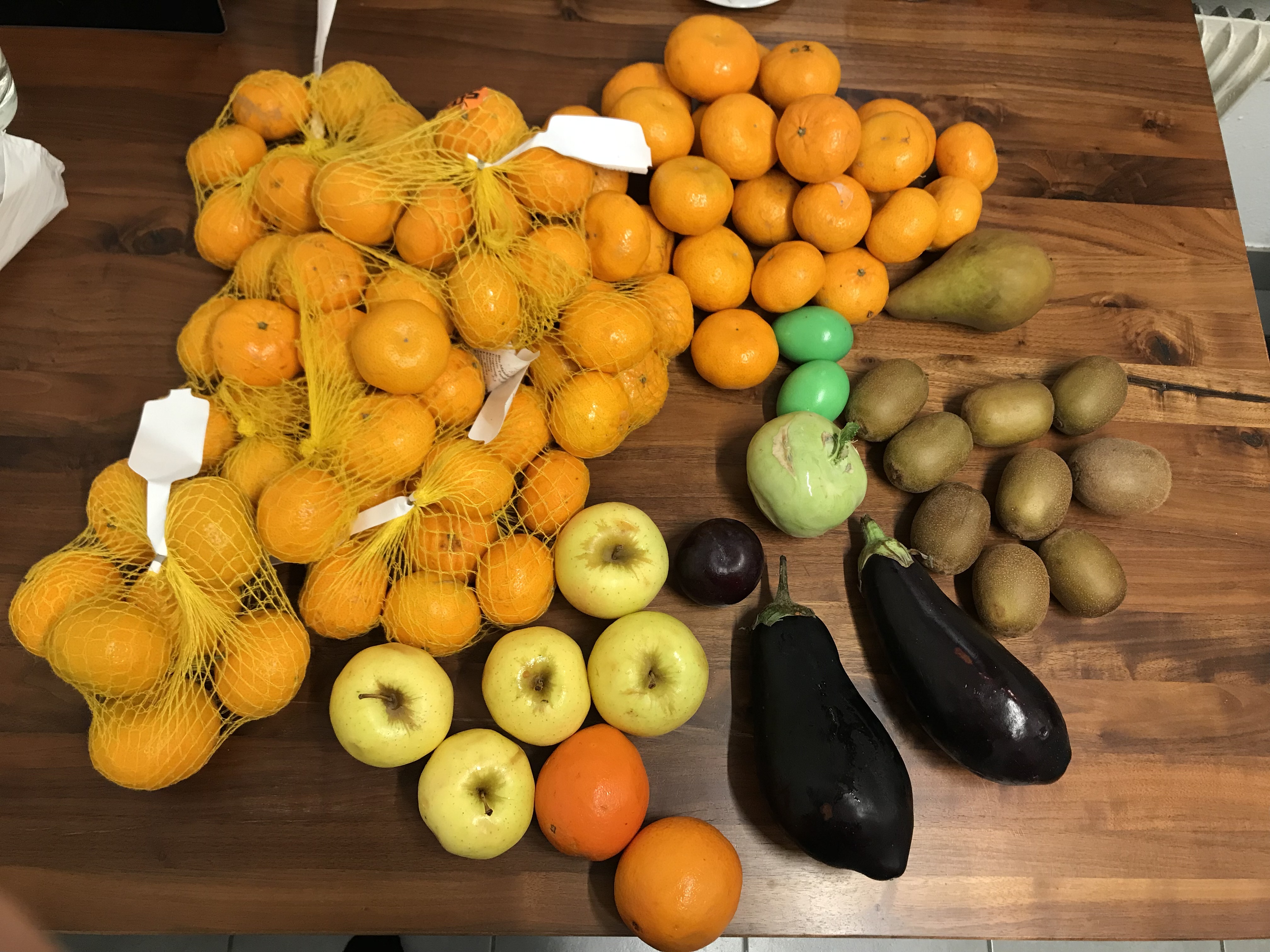 Rescued mandarins, apples, kiwis, eggplants and a pear laid out on a wooden table