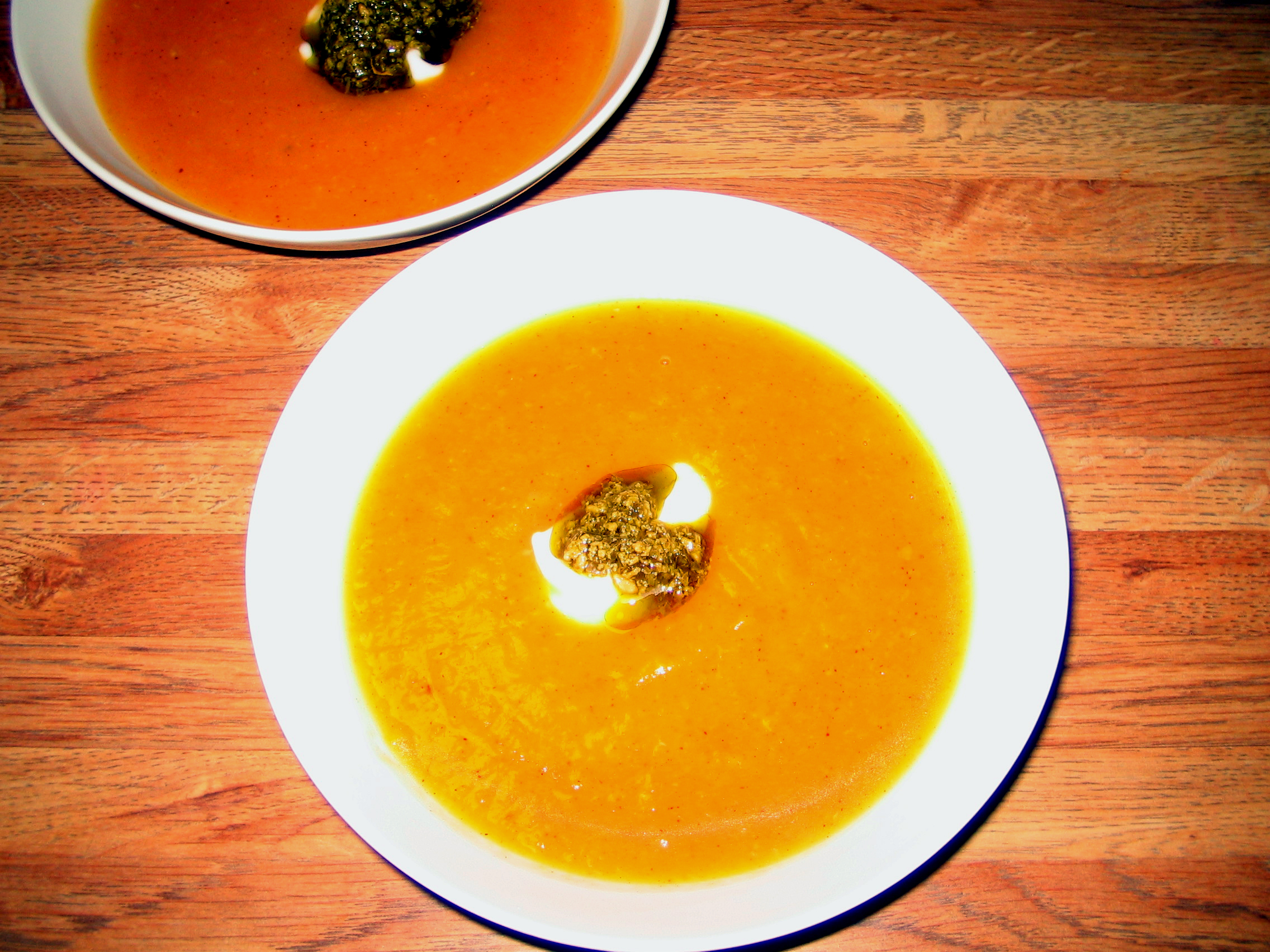A bowl of bright orange butternut squash soup with a garnish, seen from above on a wooden table
