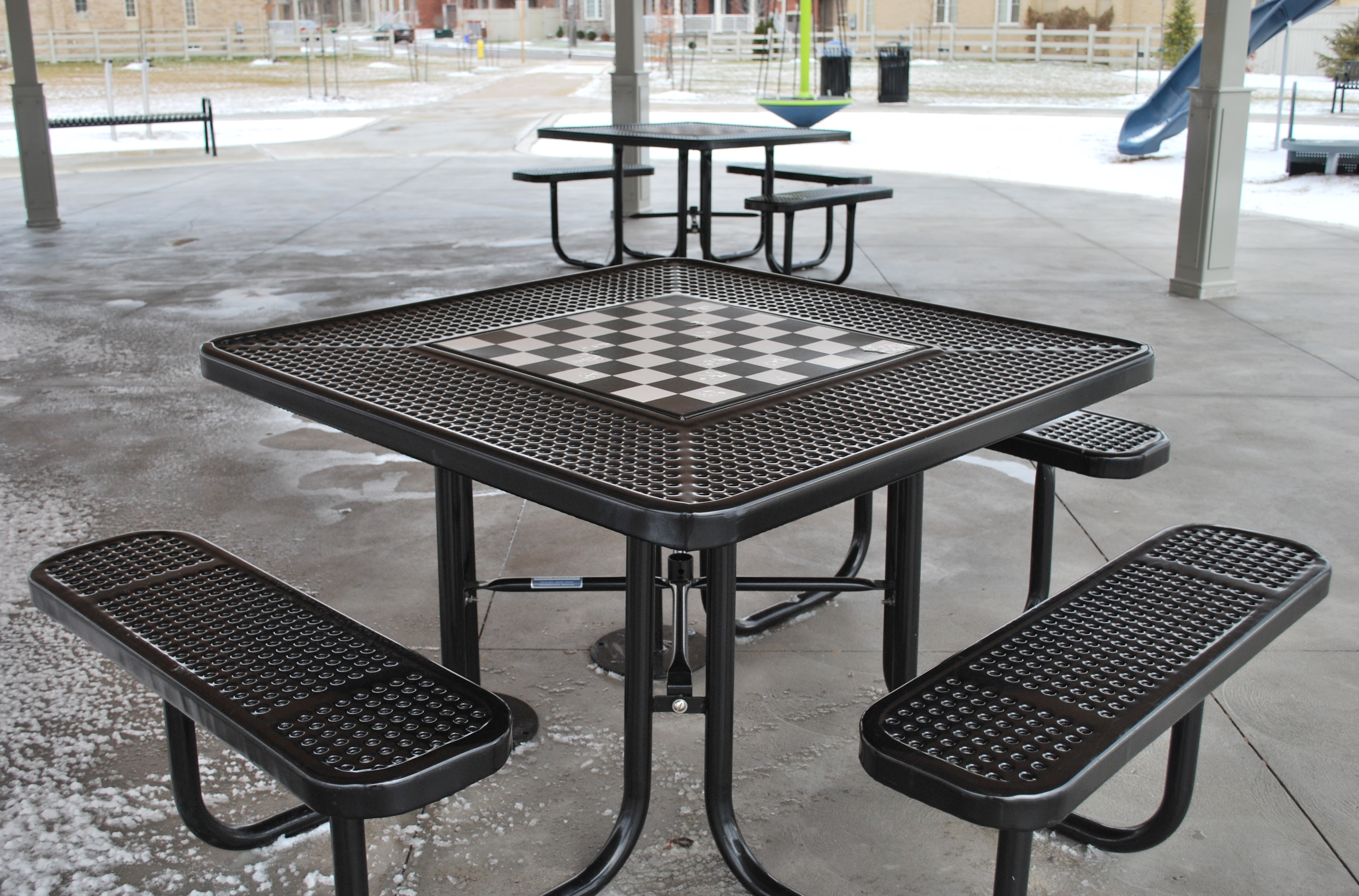 Outdoor park table with a built-in chessboard and benches under a shelter