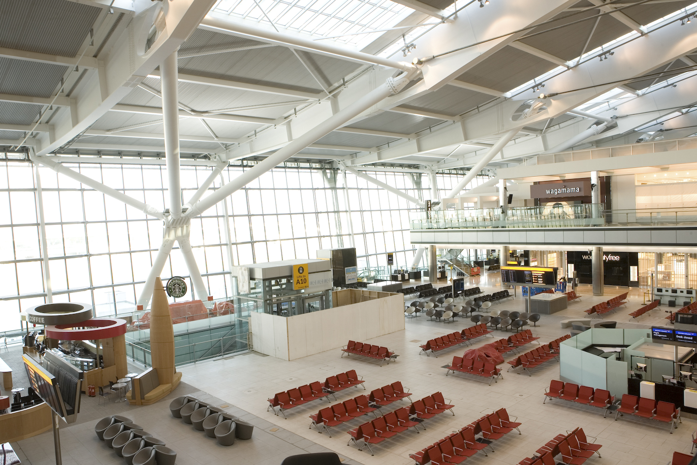 Rows of empty red seats in a bright, high-ceilinged airport gate area